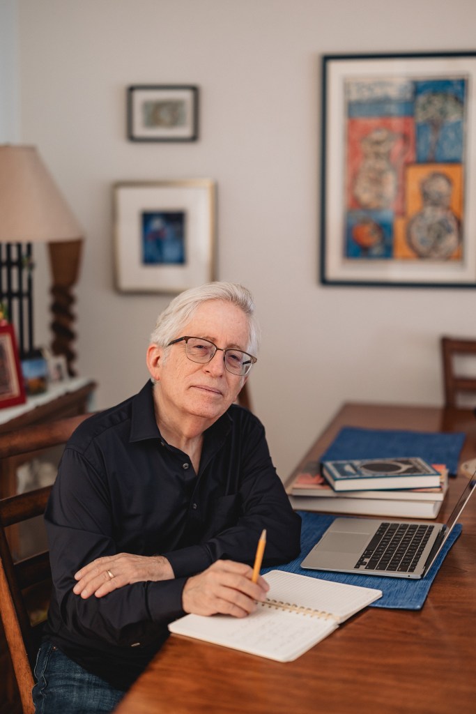 Bob Pincus, an art critic, sits at his desk with an open laptop, notebook, and a stack of art books.